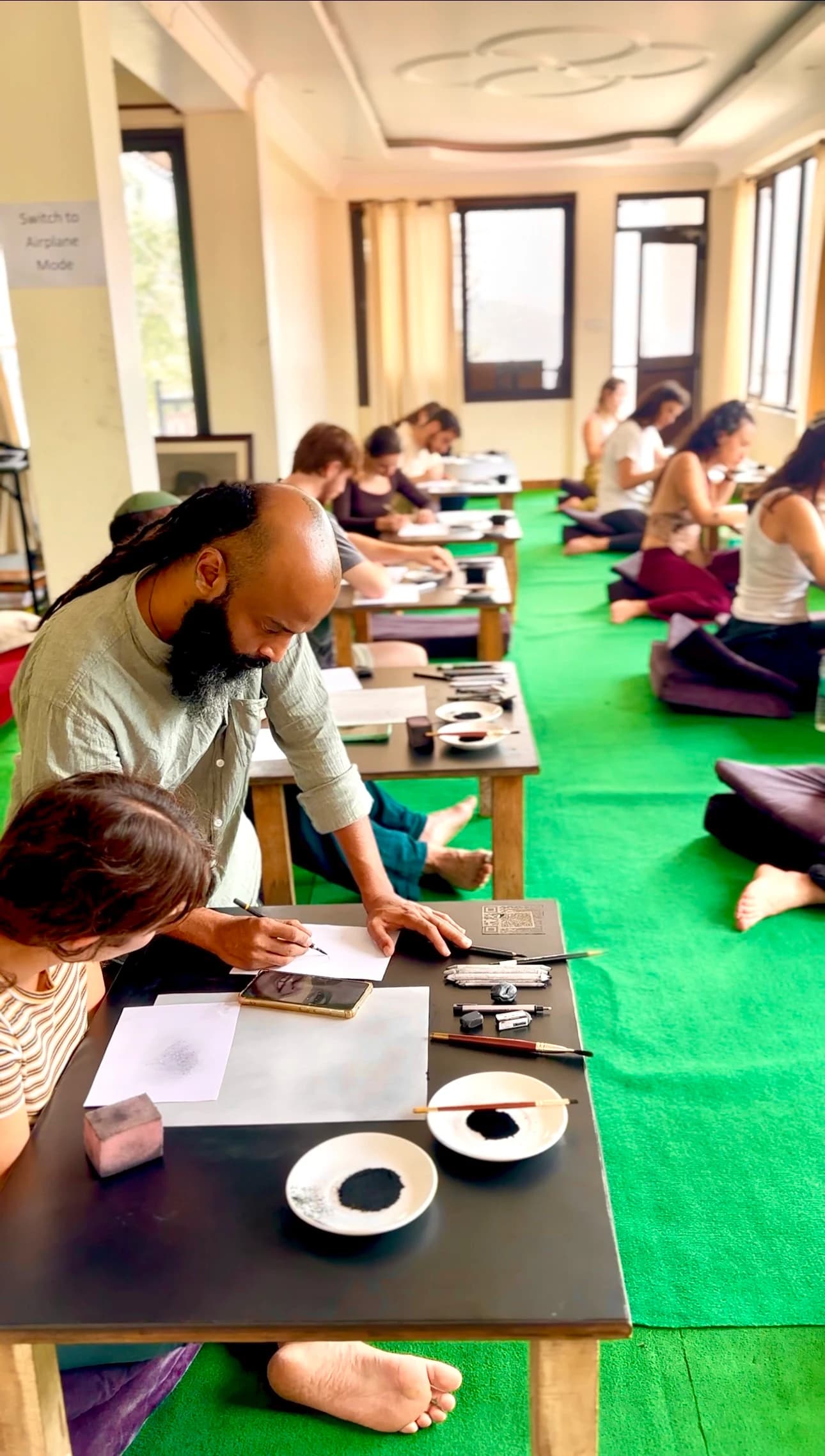 An instructor guides a participant’s charcoal sketch while other students draw in the classroom