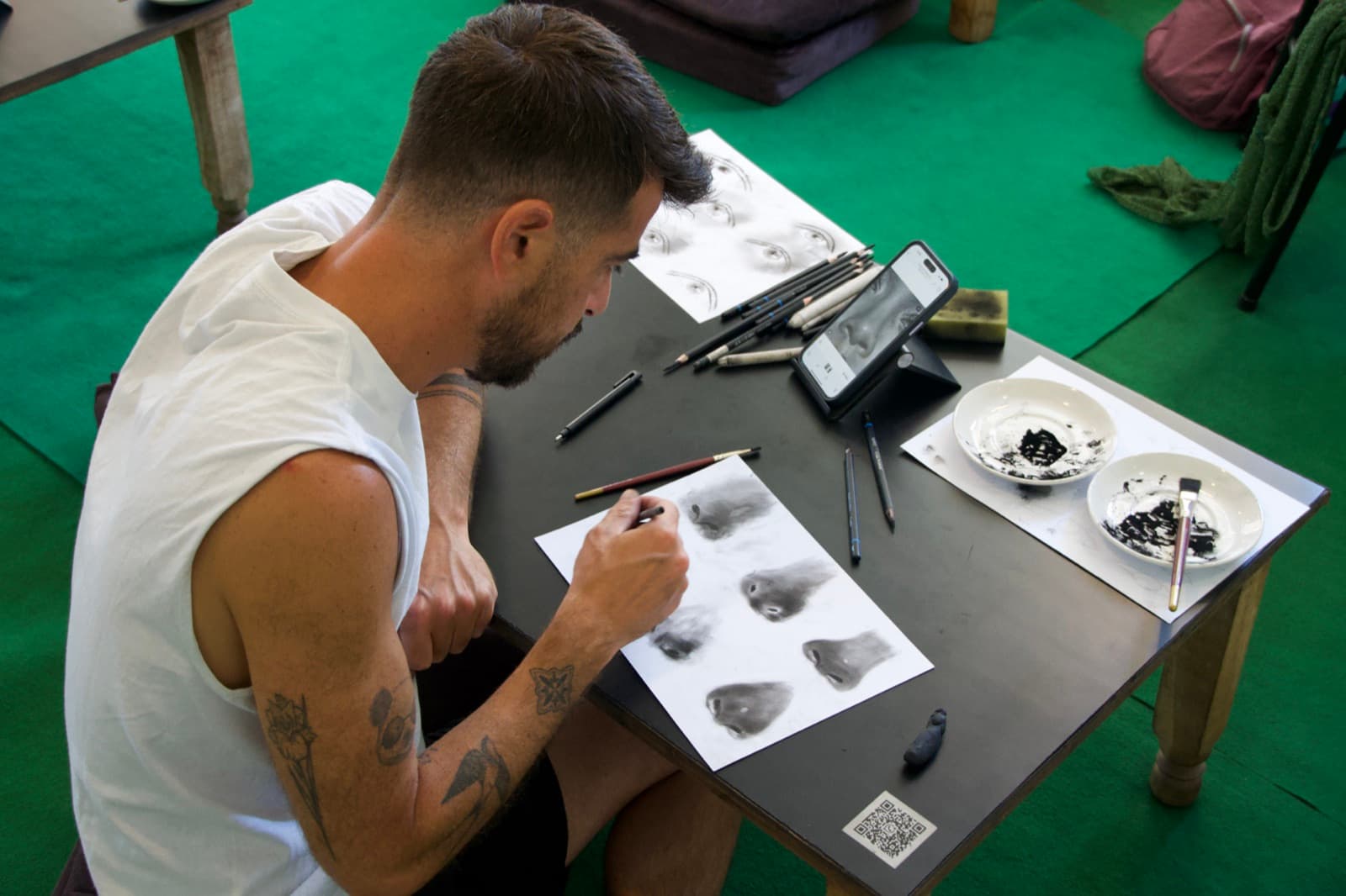Student practising charcoal eye studies with drawing tools and a reference image