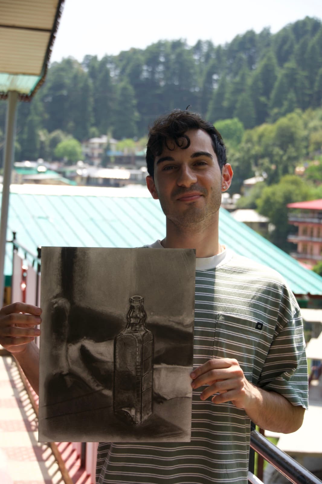 Student holding a completed charcoal still-life drawing in Dharamkot