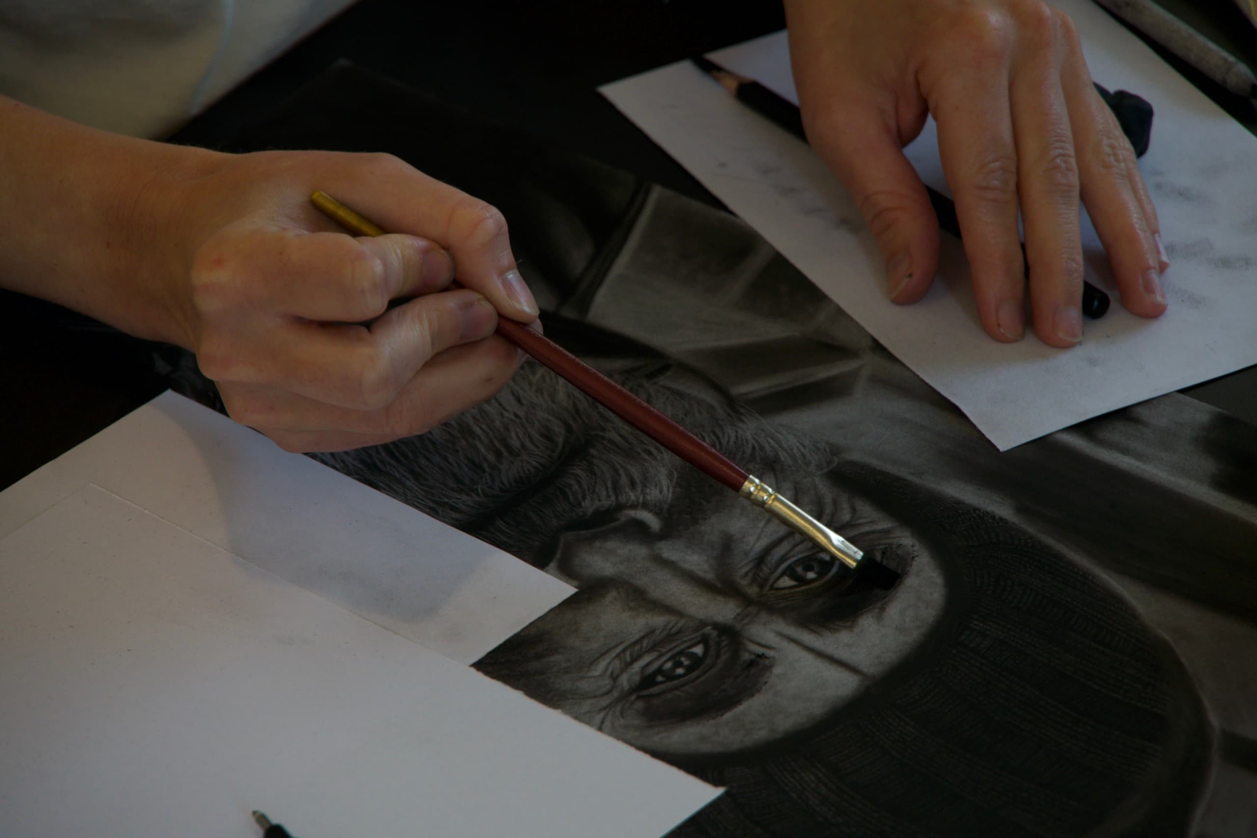 Artist refining a charcoal portrait drawing with a dry brush