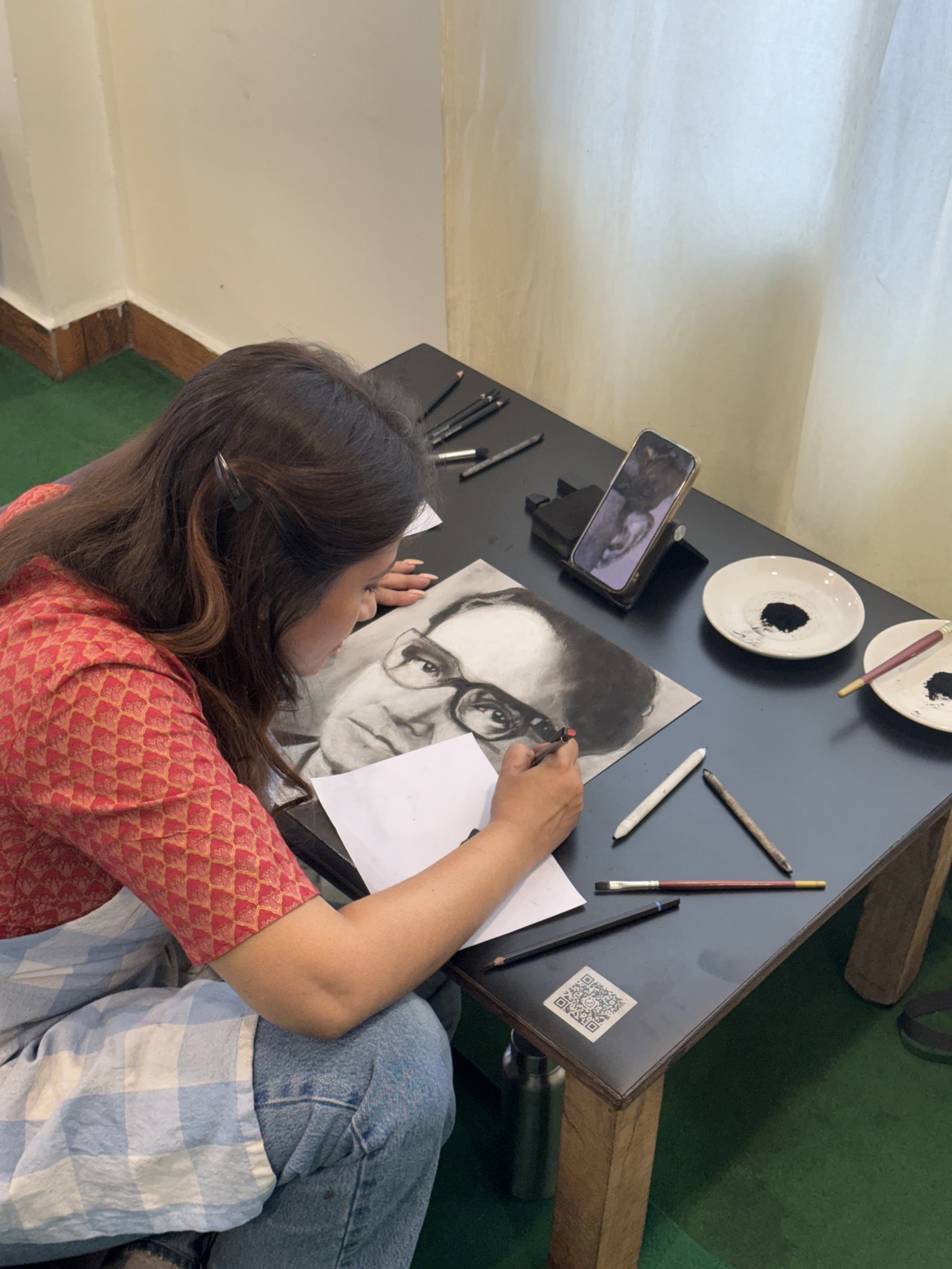 Student drawing a charcoal portrait from a reference at the studio table